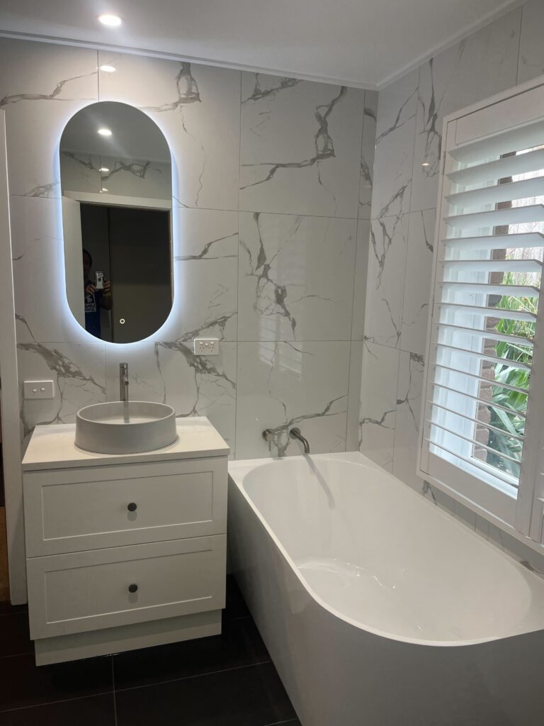 Newly renovated bathroom with luxurious white marble patterned tiles, an LED mirror and matching fittings